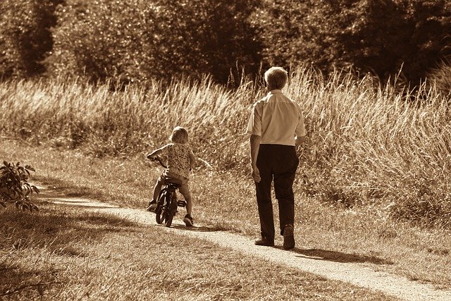 Un nonno segue un bambino che va in bicicletta su un sentiero di campagna