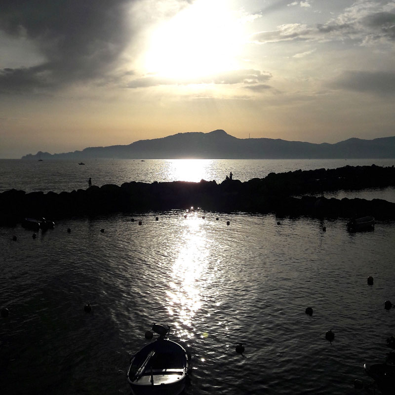 una barchetta si intravede di fronte al sole nel mare