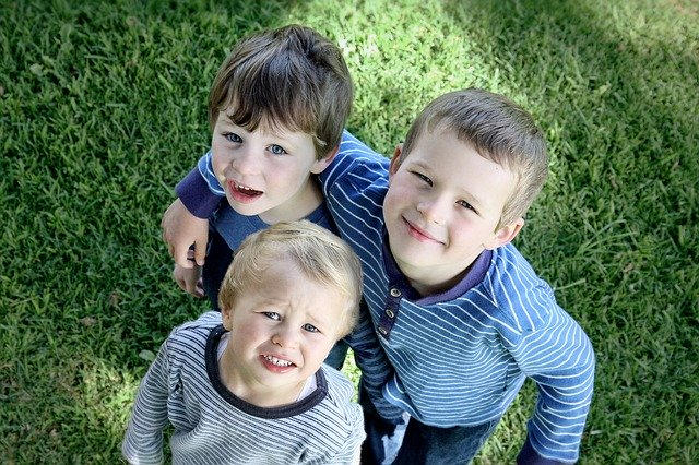 Tre bambini biondi che sembrano fratelli guardano in alto verso l'obiettivo della macchina fotografica